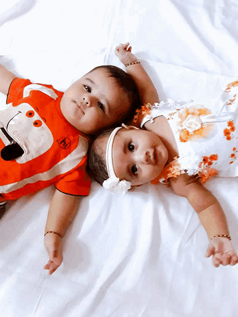 two babies are laying next to each other on a bed and one has a shirt that says ' m ' on it