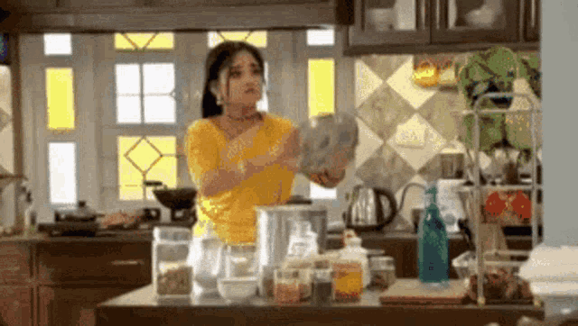 a woman in a yellow shirt is standing in a kitchen holding a plate .