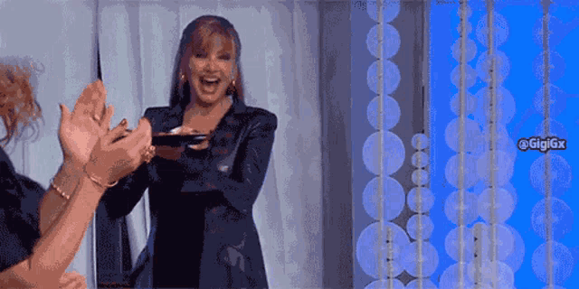 a woman in a black jacket is smiling and clapping her hands
