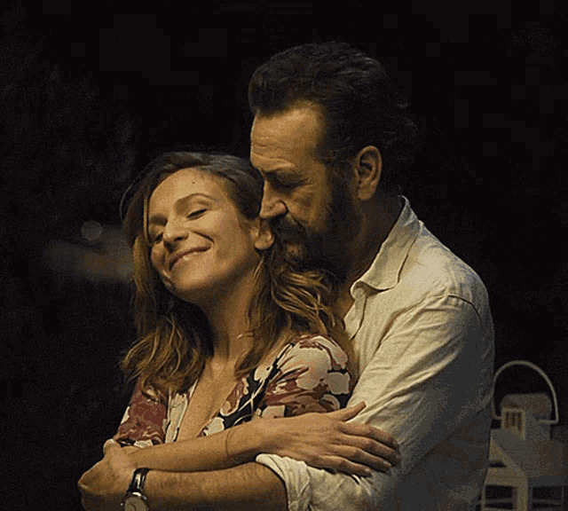 a man and woman are hugging each other and the woman is smiling