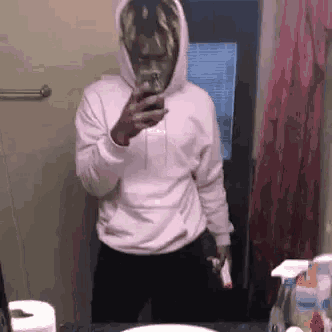 a man in a pink hoodie is taking a selfie in front of a mirror in a bathroom .