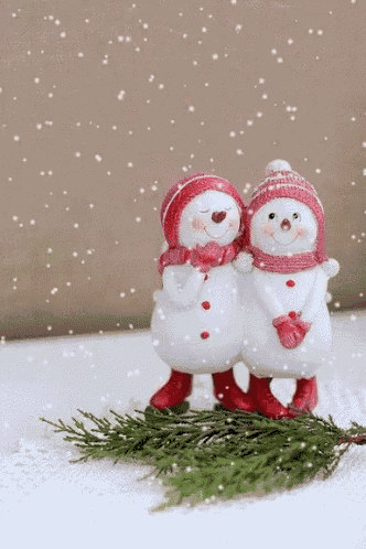 two snowmen are standing next to each other in the snow .