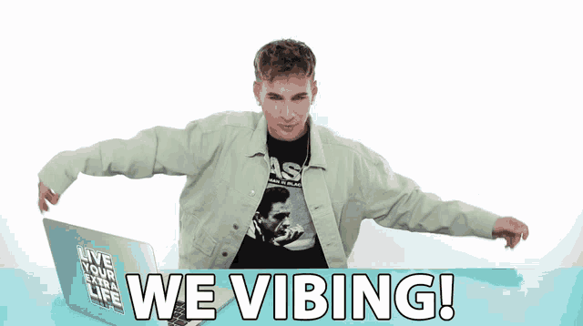 a man in a green jacket stands in front of a laptop that says " we vibing "
