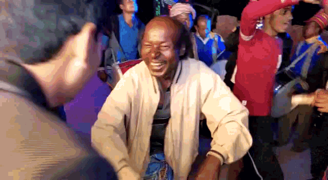 a man in a tan jacket is laughing in a crowd