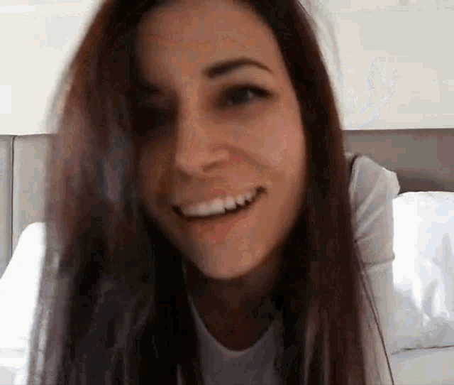 a woman with long hair is smiling and looking at the camera while sitting on a bed .