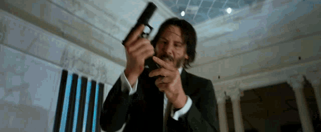 a man in a suit is holding a gun in his hand and pointing it at the camera .