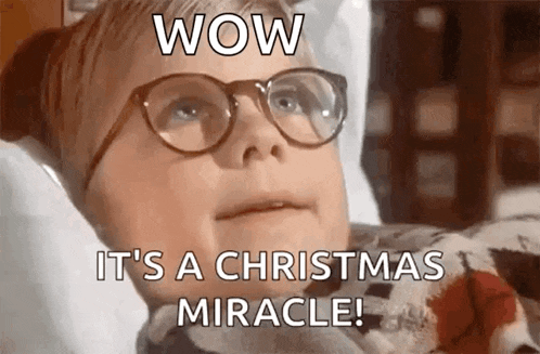 a boy wearing glasses is laying in a bed with the words `` wow it 's a christmas miracle ! ''