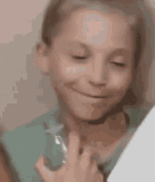 a little girl in a green shirt is holding a bottle of perfume and smiling .