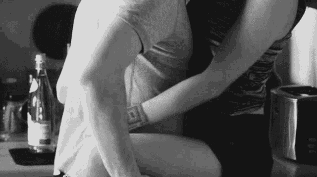 a black and white photo of a man and a woman hugging each other in a kitchen .