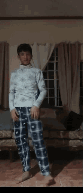 a man in plaid pajamas stands in a living room