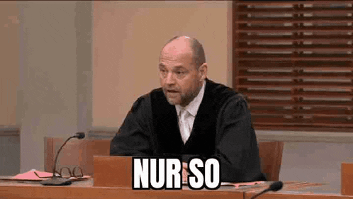 a man in a judge 's robe is sitting at a table in front of a microphone and a laptop .