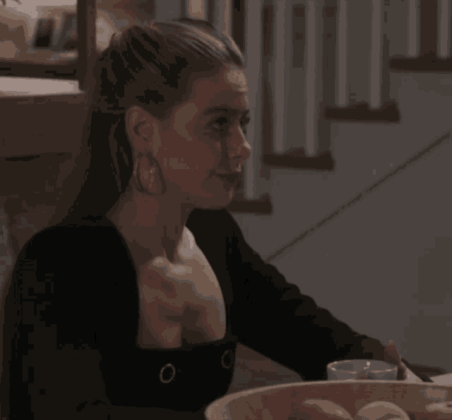 a woman wearing hoop earrings is sitting at a table with a bowl of fruit