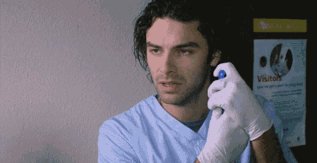 a man in a blue scrub is holding a spray bottle in front of a sign that says " visitors "
