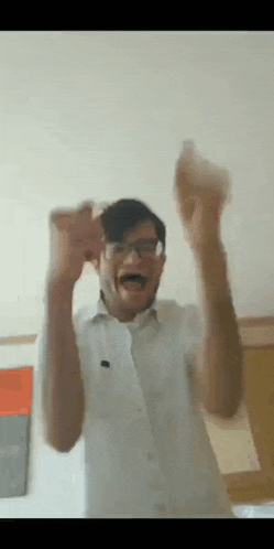 a man wearing glasses and a white shirt is holding his hands in the air .