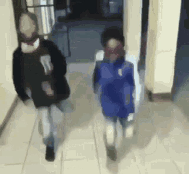 a blurry picture of two people walking down a hallway with one wearing a blue jacket