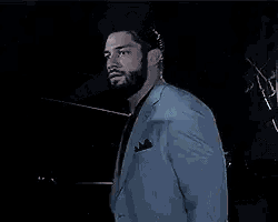 a man with a beard is wearing a blue suit jacket and black shirt .