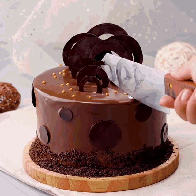 a person is cutting a chocolate cake with a knife on a wooden cutting board