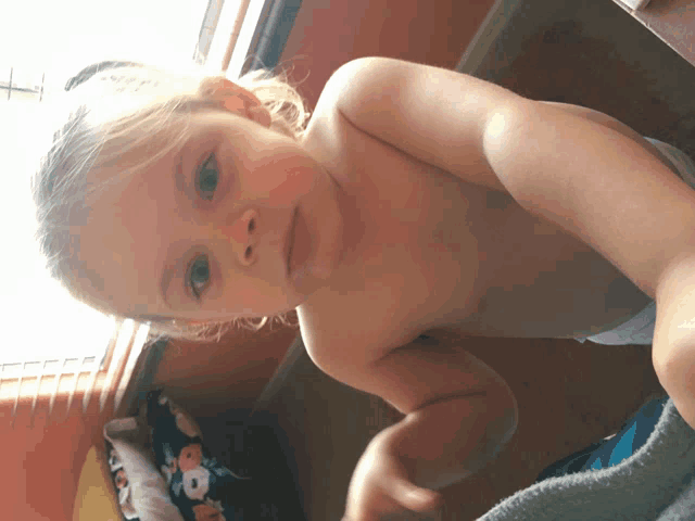a little girl without a shirt looks at the camera