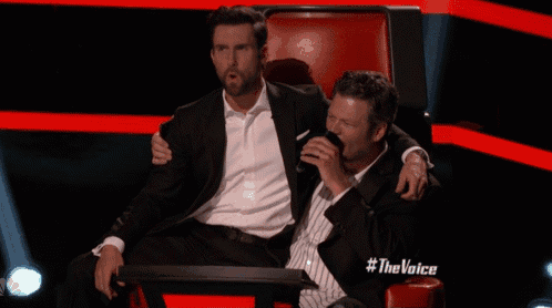two men are sitting next to each other on a red chair with #thevoice written on it
