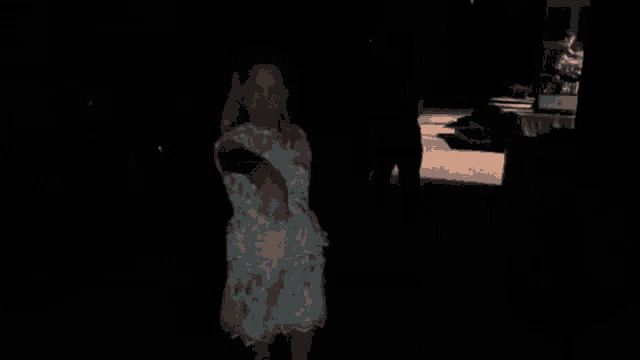 a little girl in a white dress is standing in a dark room holding a shoe .