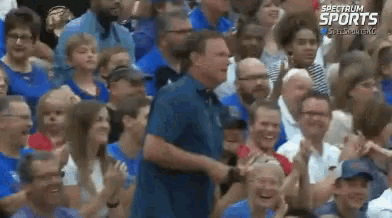 a man in a blue shirt is standing in front of a crowd of people with spectrum sports written on the bottom right