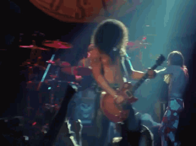 a man with long hair is playing a guitar in front of a drum set