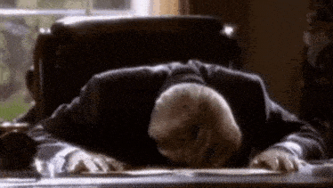 a man is laying his head on a desk with his hands on the desk .
