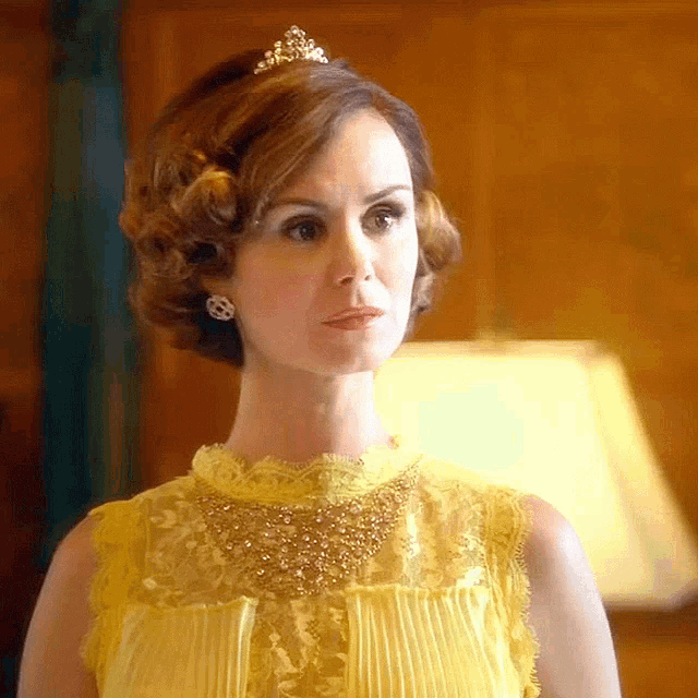 a woman wearing a yellow dress and a tiara looks at the camera