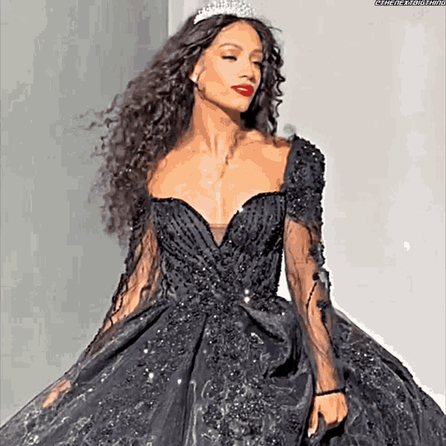 a woman in a black dress and tiara is standing on a runway .
