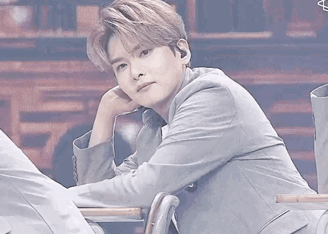 a young man in a suit is sitting at a desk with his hand on his face .