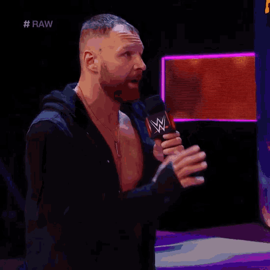a man with a beard is holding a microphone in front of a screen that says raw