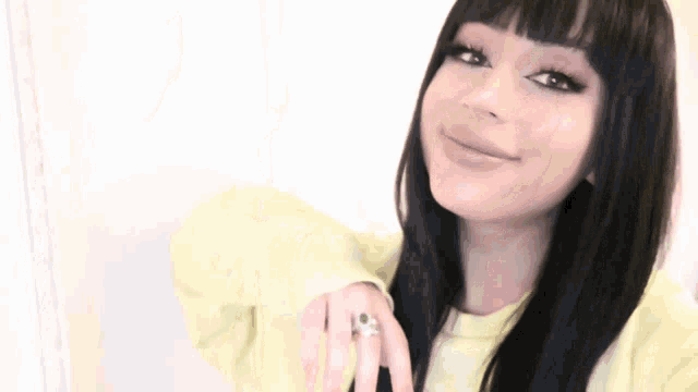 a woman with long black hair and bangs is making a peace sign with her hand .