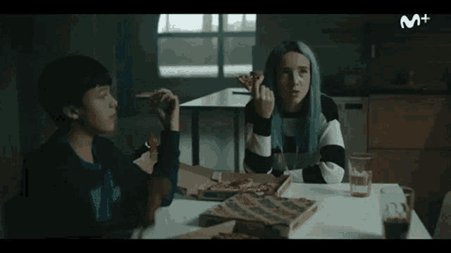 a boy and a girl are sitting at a table with pizza boxes and a glass of soda .