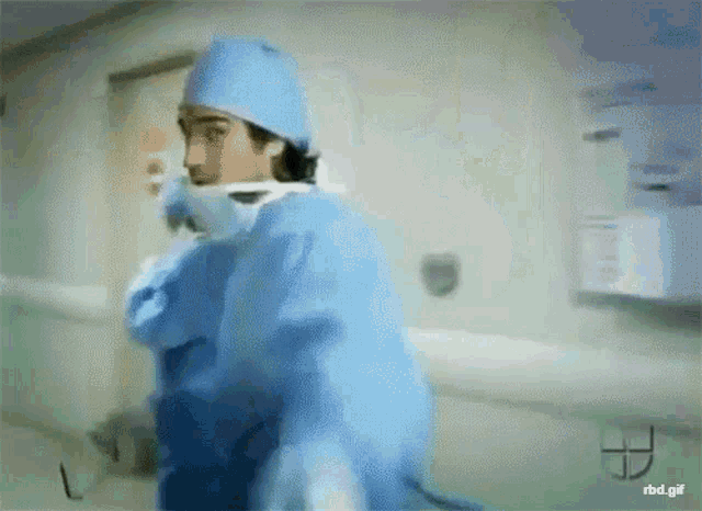 a man in a surgical gown is walking down a hallway with rbd.gif below him