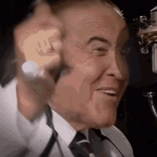 a man in a suit and tie is talking into a microphone and smiling .