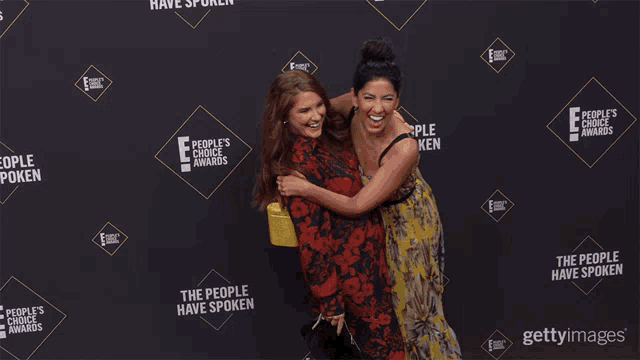 two women are standing on a red carpet that says the people have spoken