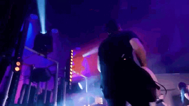 a man in a black shirt is walking on a stage with purple lights behind him