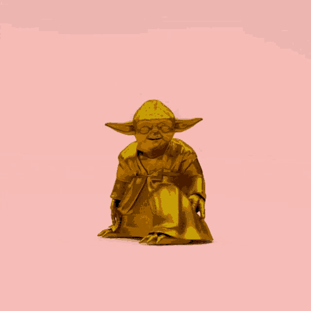 a gold statue of yoda is sitting on a pink background