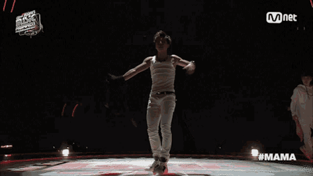 a man in a white tank top is dancing on a stage with a mnet logo in the background