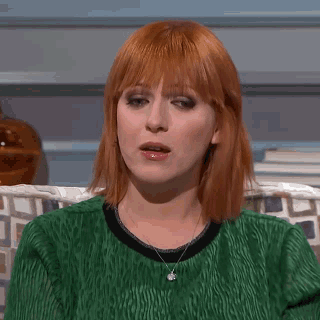 a woman with red hair is wearing a green top and a necklace