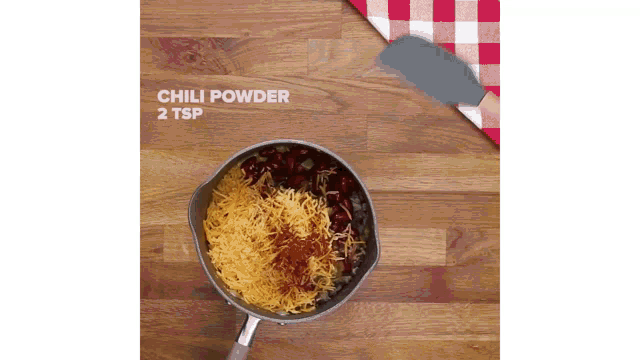 a pot filled with chili powder , cheese , and beans on a wooden table .