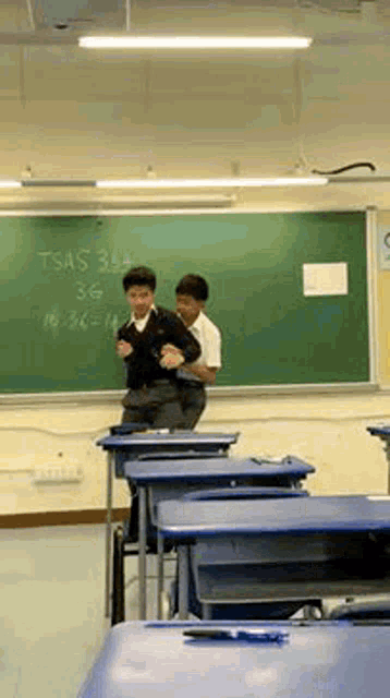 two boys are dancing in front of a blackboard that says tsas 36