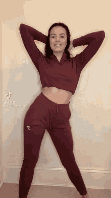 a woman in a crop top and leggings is standing with her hands behind her head ..