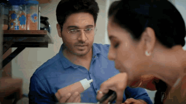 a man in a blue shirt is holding a bottle of sauce and talking to a woman in a kitchen