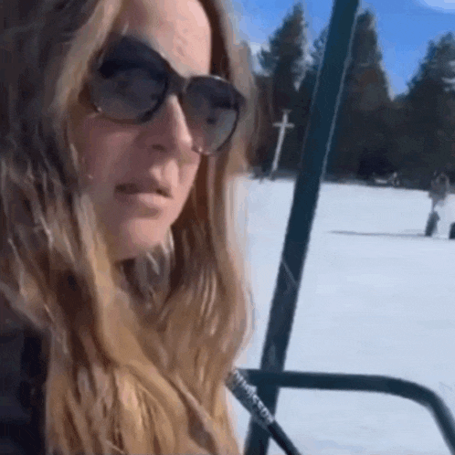 a woman wearing sunglasses is riding a ski lift