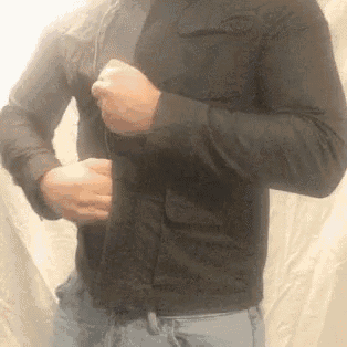 a man in a black shirt and blue jeans is adjusting his jacket