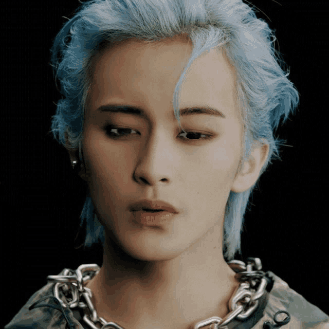 a close up of a person with blue hair and a chain around their neck