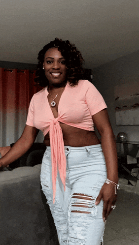 a woman in a pink crop top and ripped jeans smiles for the camera