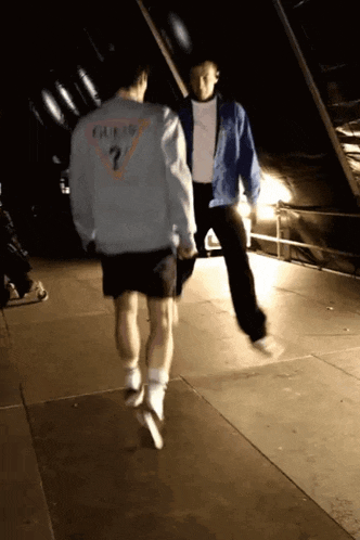 a man wearing a guess jacket is jumping in the air with another man