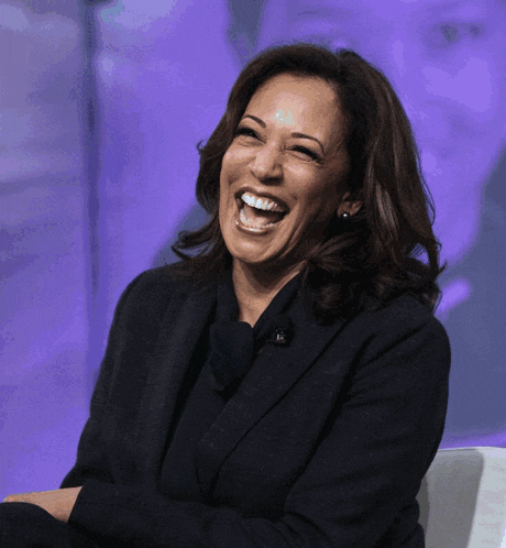 a woman in a black suit is laughing with a purple background
